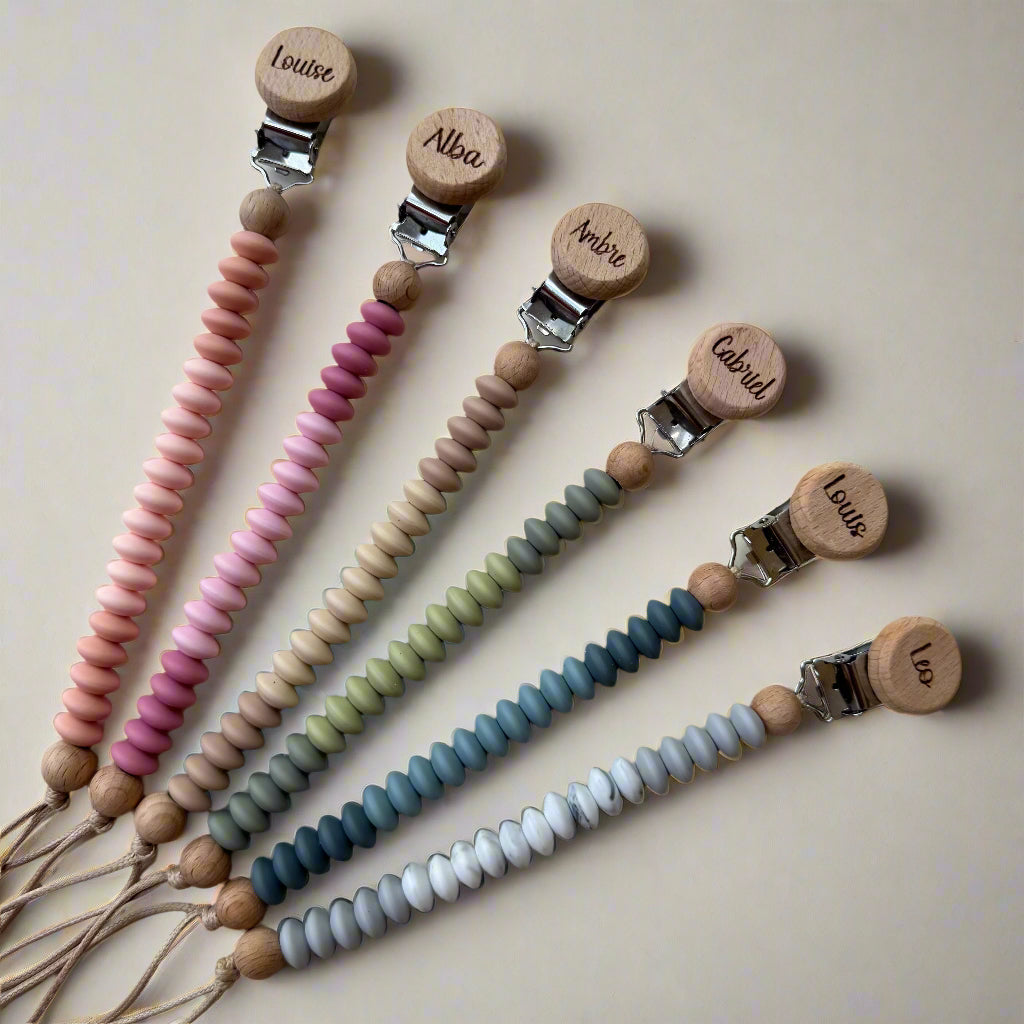 Set of pacifier clips with colorful beads and engraved names on a light background